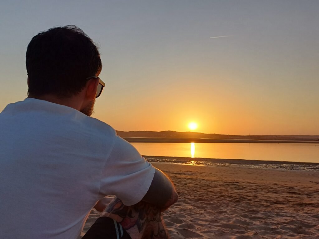 Man sitting on the beach enjoying a colorful sunset in Alvor, Algarve