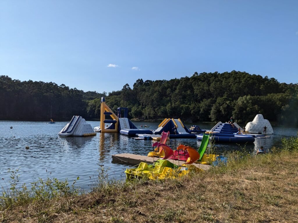 View of Fratelli Water Park at Barragem da Queimadela, featuring inflatable slides and obstacles floating on the reservoir's water.