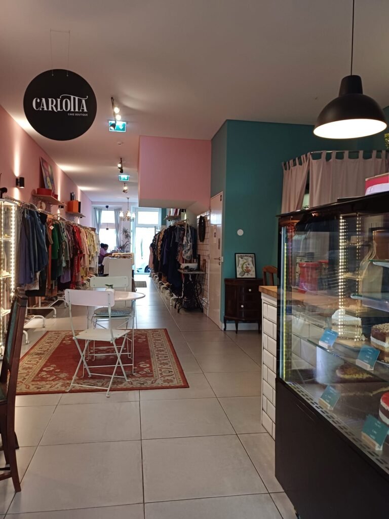 Shared space of Carlotta Cake Boutique and Com Sotaque, featuring a cozy seating area with cakes on display and racks of secondhand clothing in the background.